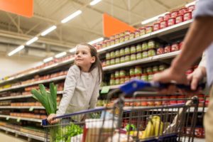 Young girl hanging on a shopping cart while scouting the food aisle.