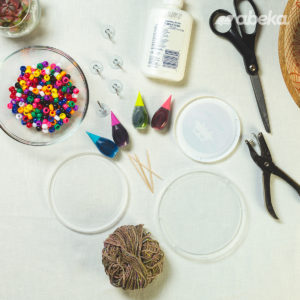 A plastic food lid, glue, food coloring, toothpicks, a hole punch, scissors, string, beads, and suction cups