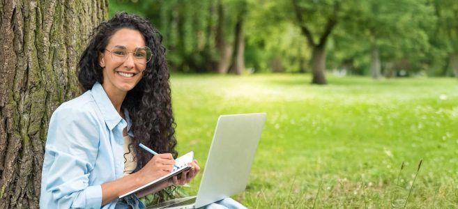 Woman smiling at camera sitting outside while working on computer.