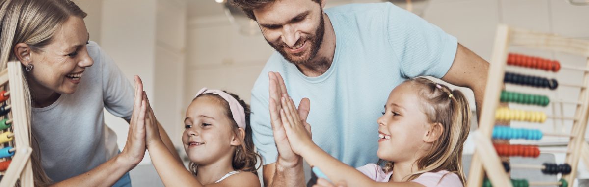 Smiling parents high-fiving their two daughters while doing a lesson at a table