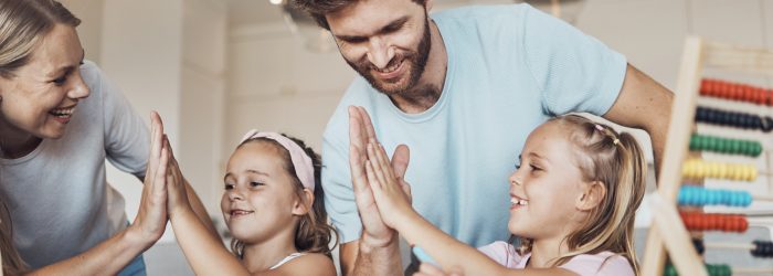 Smiling parents high-fiving their two daughters while doing a lesson at a table