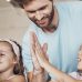 Smiling parents high-fiving their two daughters while doing a lesson at a table