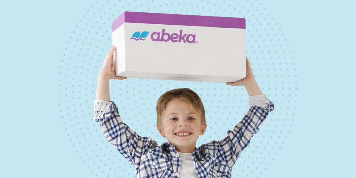 A young boy that is smiling holds up a white and purple box that says “Abeka.”