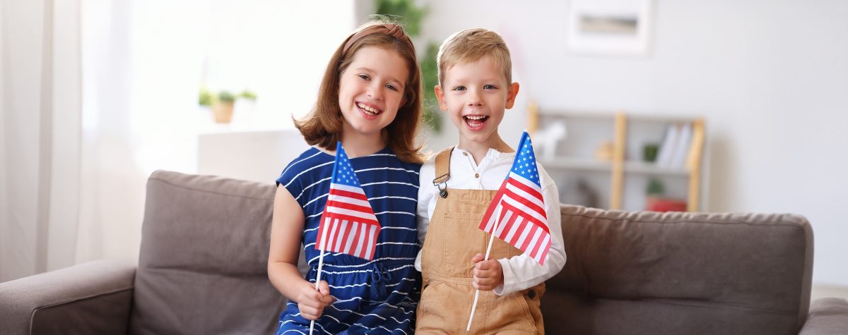 A boy and a girl smile while holding American flags.