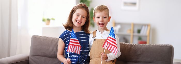 A boy and a girl smile while holding American flags.